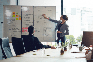 Eduvalue Singapore strategic planning session showing a woman presenting business goals on a whiteboard to colleagues.